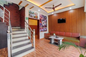 A lobby with a staircase, a sofa, a television, and a wall with pictures. - Hotel Amishi (Haridwar)