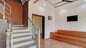 A staircase with metal railings and a wooden floor, leading to a room with a brown leather sofa and a flat-screen TV mounted on the wall. - Hotel Amishi (Haridwar)