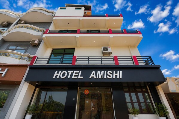 Egy „HOTEL AMISHI” nevű szálloda, modern építészeti stílusban, számos eréllyel és nyitott, tiszta égbolttal.