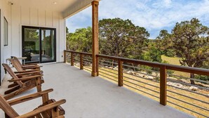 A covered outdoor area with wooden chairs, a glass door leading inside, and a view of trees and landscape.
