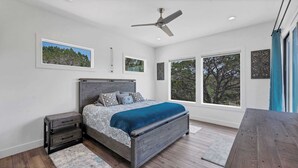 A bedroom with a bed, a nightstand, a ceiling fan, and large windows.