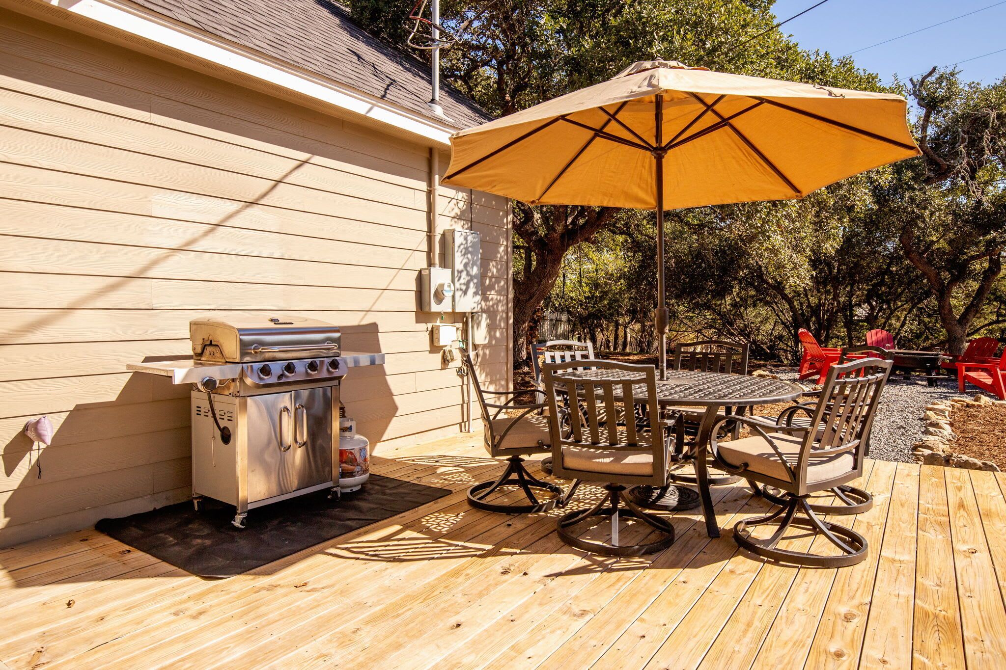 An outdoor patio with a grill, a table, and chairs under a large umbrella.