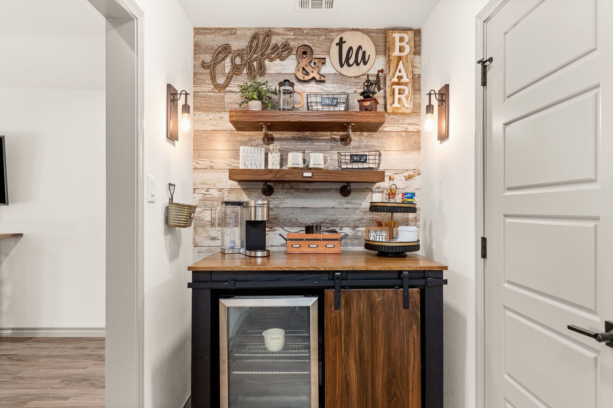 A kitchen area with wooden shelves, a coffee station, and a refrigerator.