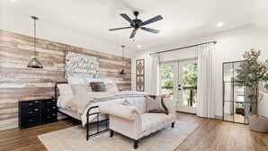 Ein Schlafzimmer mit einem Bett, einer Couch, einem Deckenventilator, einer Holzwand und einem großen Fenster.