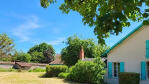 Una casa de exterior blanco con contraventanas azules, rodeada de un patio césped y varios árboles.