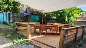 Una terraza de madera con mesa y sillas, rodeada de grava y follaje.