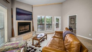 A living room with a fireplace, a sofa, a coffee table, and a painting on the wall. - Enjoy the Full River | Fire Pit & Deck | Sleeps 12 (Seguin)