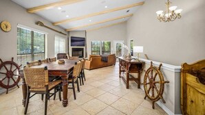 A spacious dining area with a wooden table and chairs, a sofa, and a chandelier. - Enjoy the Full River | Fire Pit & Deck | Sleeps 12 (Seguin)
