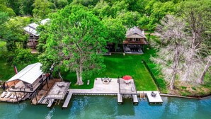 A lakeside property with a dock, a large house, and a well-maintained lawn. - Enjoy the Full River | Fire Pit & Deck | Sleeps 12 (Seguin)