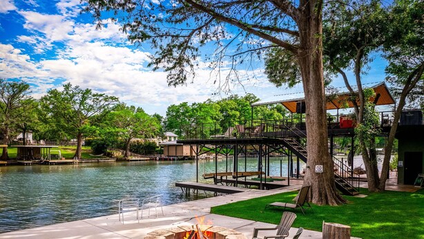 Un patio junto al lago con un hogar para fogata, asientos al aire libre y un muelle que se adentra en el agua.