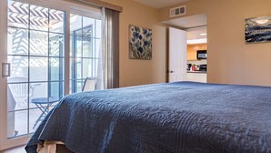 A bedroom with a large bed, a sliding glass door to a patio, and a view of the kitchen. - Cozy House, Pool, Spa, Tennis & Pickleball Courts (Tempe)