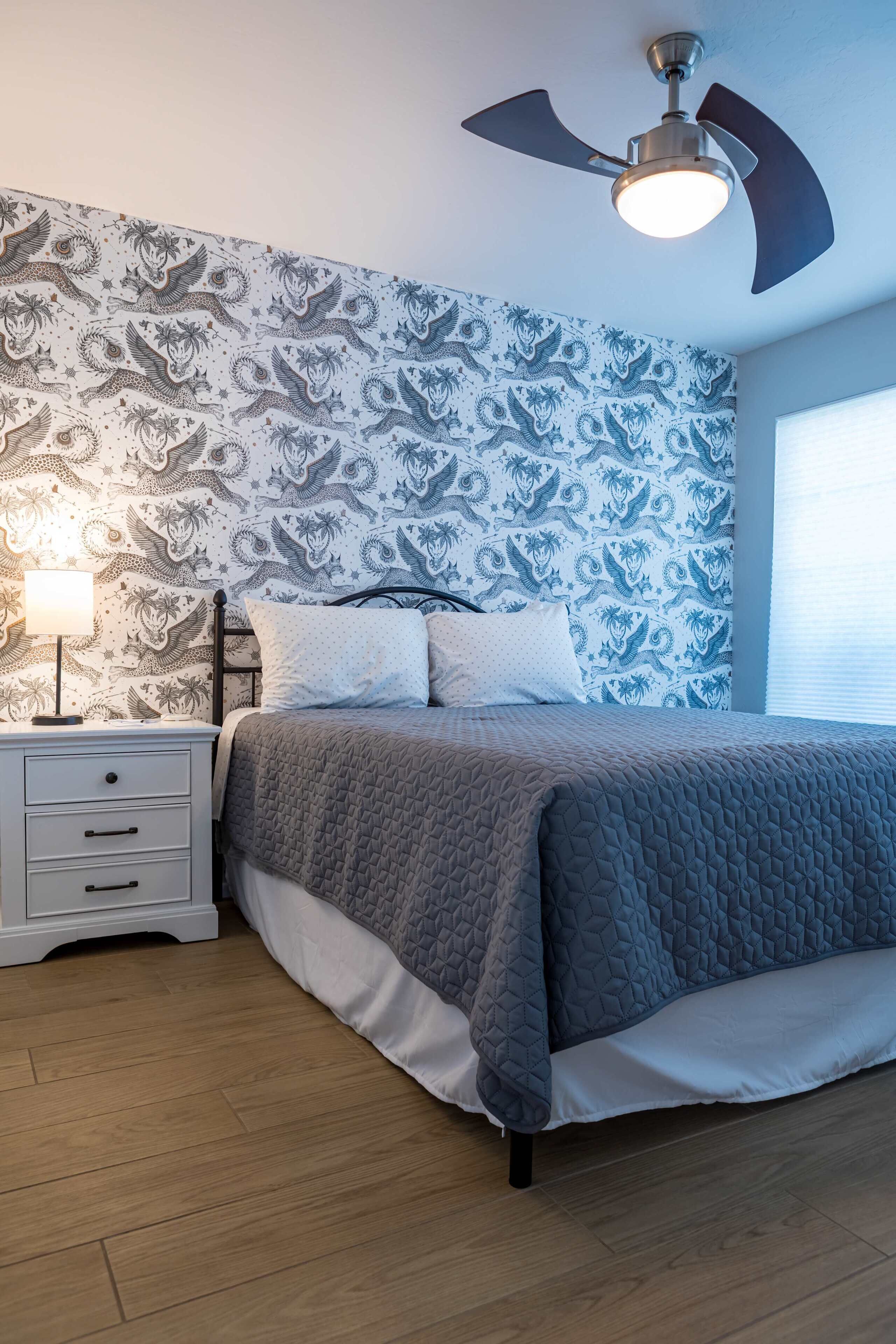 Een slaapkamer met een bed, nachtkastje en plafondventilator.