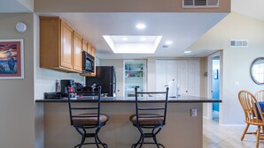 A kitchen with a central island, two bar stools, wooden cabinets, a black refrigerator, and a window overlooking the room. - Cozy House, Pool, Spa, Tennis & Pickleball Courts (Tempe)