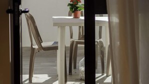 Eine Terrassengruppe im Freien mit einem weißen Tisch, zwei Stühlen, einem Blumentopf und einem bunten, gestreiften Sonnenschirm.