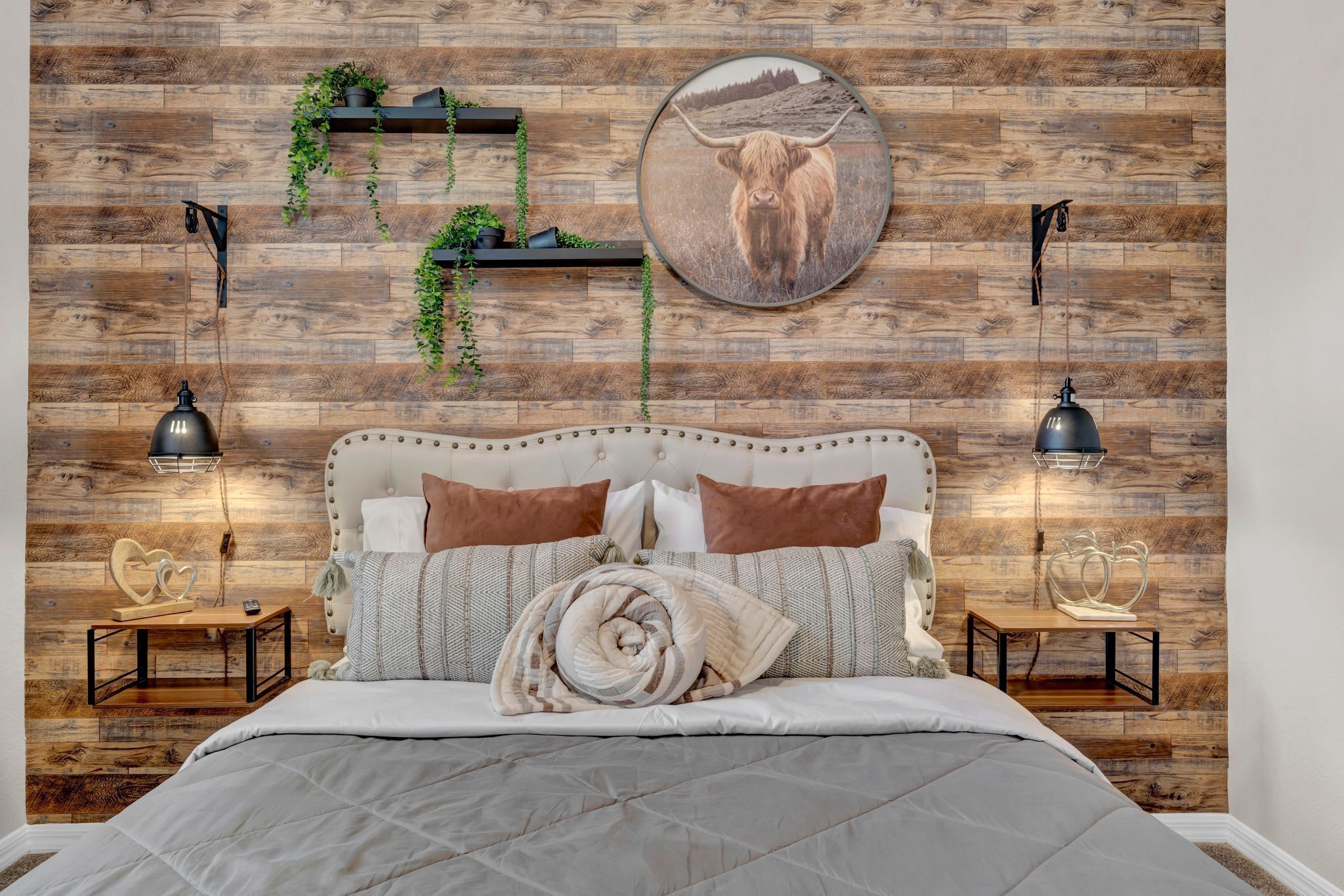 Une chambre avec un mur en bois, un tableau rond représentant un taureau, deux tables de chevet avec des lampes et un lit recouvert d’une courtepointe.