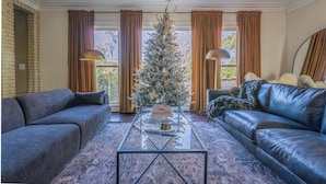 A living room with a glass coffee table, two sofas, a Christmas tree, and large windows with curtains. - Midtown Family Getaway w/ Game Room & Backyard (Columbus)