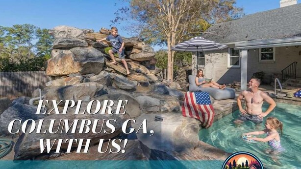A pool with rocks, a flag, and people. - Midtown Family Getaway w/ Game Room & Backyard (Columbus)