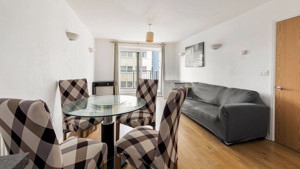 Un salon moderne avec une table en verre, des fauteuils à carreaux, un canapé gris et une porte en bois.