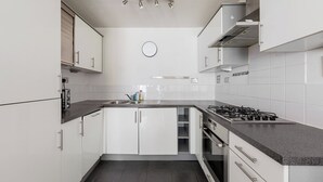 Une cuisine moderne avec des meubles blancs, un plan de travail noir, une cuisinière à gaz et un four encastré.