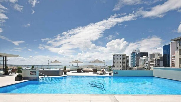 Une piscine sur le toit, agrémentée de chaises longues et de parasols, offrant une vue panoramique sur la ville.
