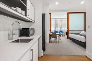 Moderni hotellihuone, jossa on pieni keittiö, ruokailutila ja sänky.