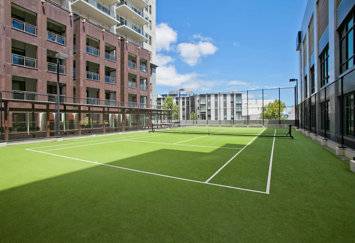 Ein Tennisplatz mit Netz, umgeben von Gebäuden mit Balkonen und Fenstern.
