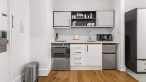 Une cuisine compacte équipée d’un four à micro-ondes, d’un four et d’un réfrigérateur, avec des meubles blancs et une petite poubelle.