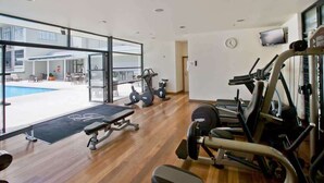 Cette salle de sport est équipée de machines de cardio, de poids libres et d’un banc. Elle possède de grandes fenêtres et offre une vue sur un espace extérieur avec une piscine.
