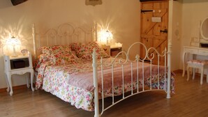 Een slaapkamer met een bloemenbedekking, een bed met een wit metalen frame, een houten deur en een klein nachtkastje met een lamp.