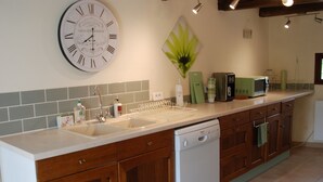 Een keuken met houten kastjes, een witte vaatwasser, een groene magnetron en een wandklok.
