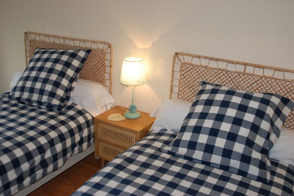 A room with two single beds, each with a checkered bedspread and matching pillows. There is a nightstand with a lamp between the beds.