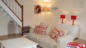 Een woonkamer met een trap, een bank met gestreepte kussens, een witte salontafel en een rode geruite plaid.