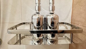 Un baño con un plato de ducha cromado que contiene dos botellas de gel de ducha y champú.