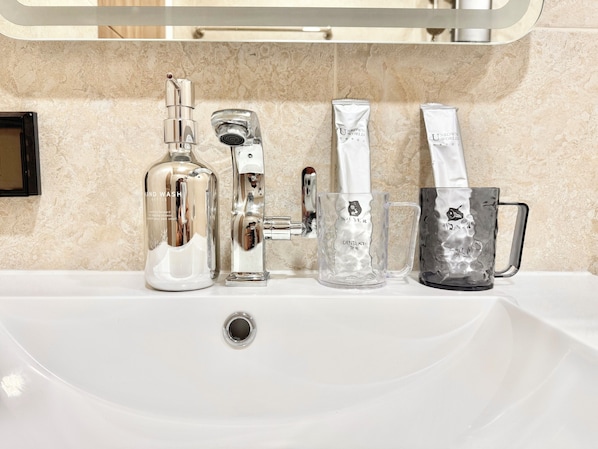 Un lavabo con una botella de jabón para manos, un grifo, un vaso y un recipiente de vidrio con asa.