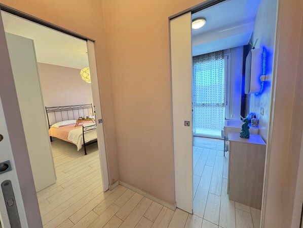 Habitación de hotel con cama, baño con espejo y lavamanos, y pasillo con puerta que da a otra habitación.