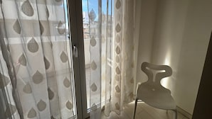 A room with a sliding glass door with a leaf-patterned sheer curtain, a white chair, and a view of buildings outside. - Casa Helios by Ca-sa Check (Chioggia)