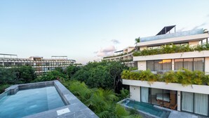 Un hotel moderno con piscina en la azotea, abundante vegetación y varios balcones.