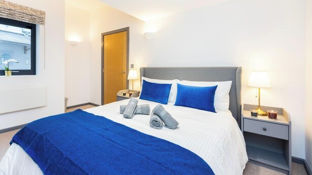 Habitación de hotel con cama, mesita de noche, lámpara y ventana con vistas.