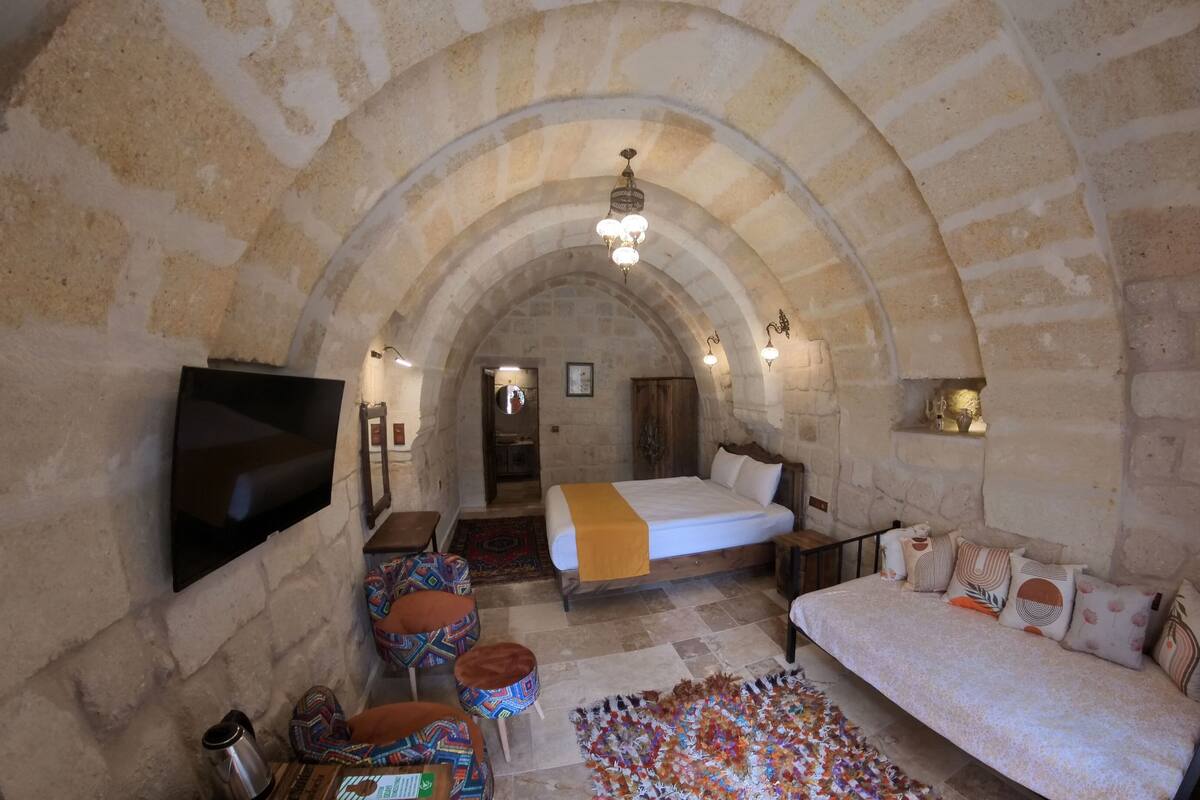 Une pièce aux murs de pierre, avec un lit, un canapé, une télévision et une petite table.