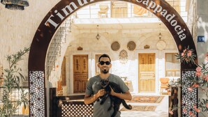 Un hombre sosteniendo un gato en la entrada de la posada Timur, Cappadocia, con tres perros al frente.