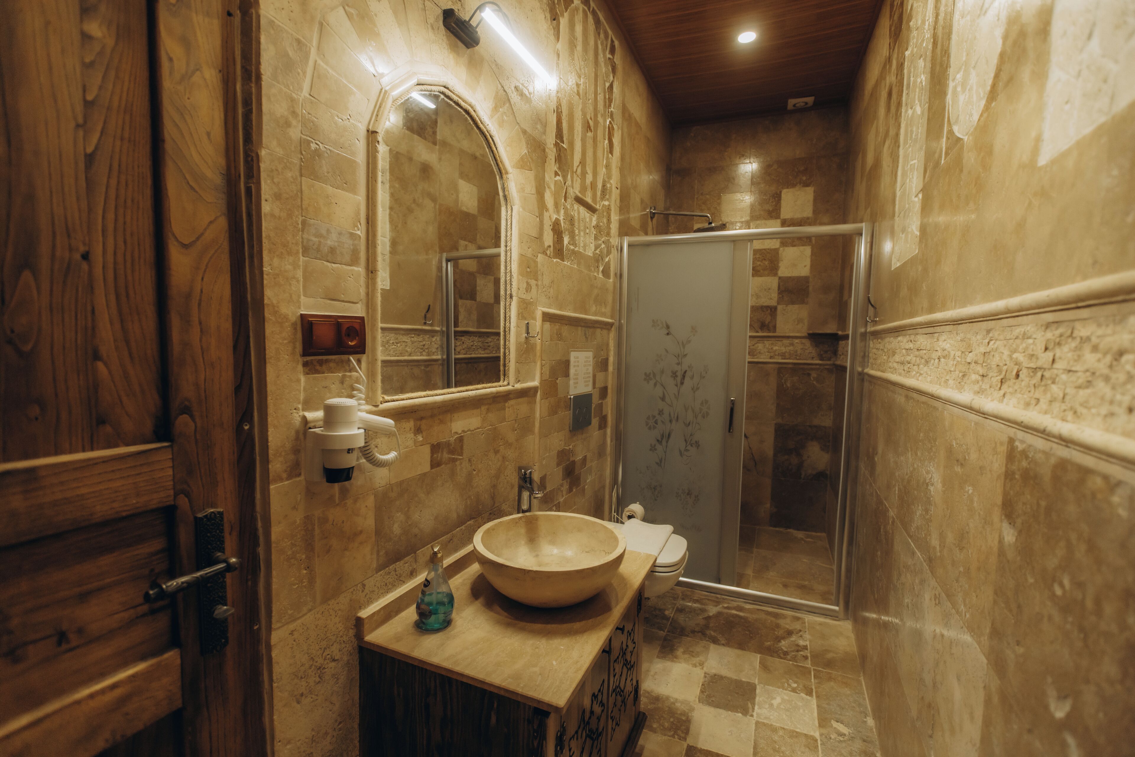A bathroom with a wooden vanity, a large mirror, a beige sink, and a shower area.