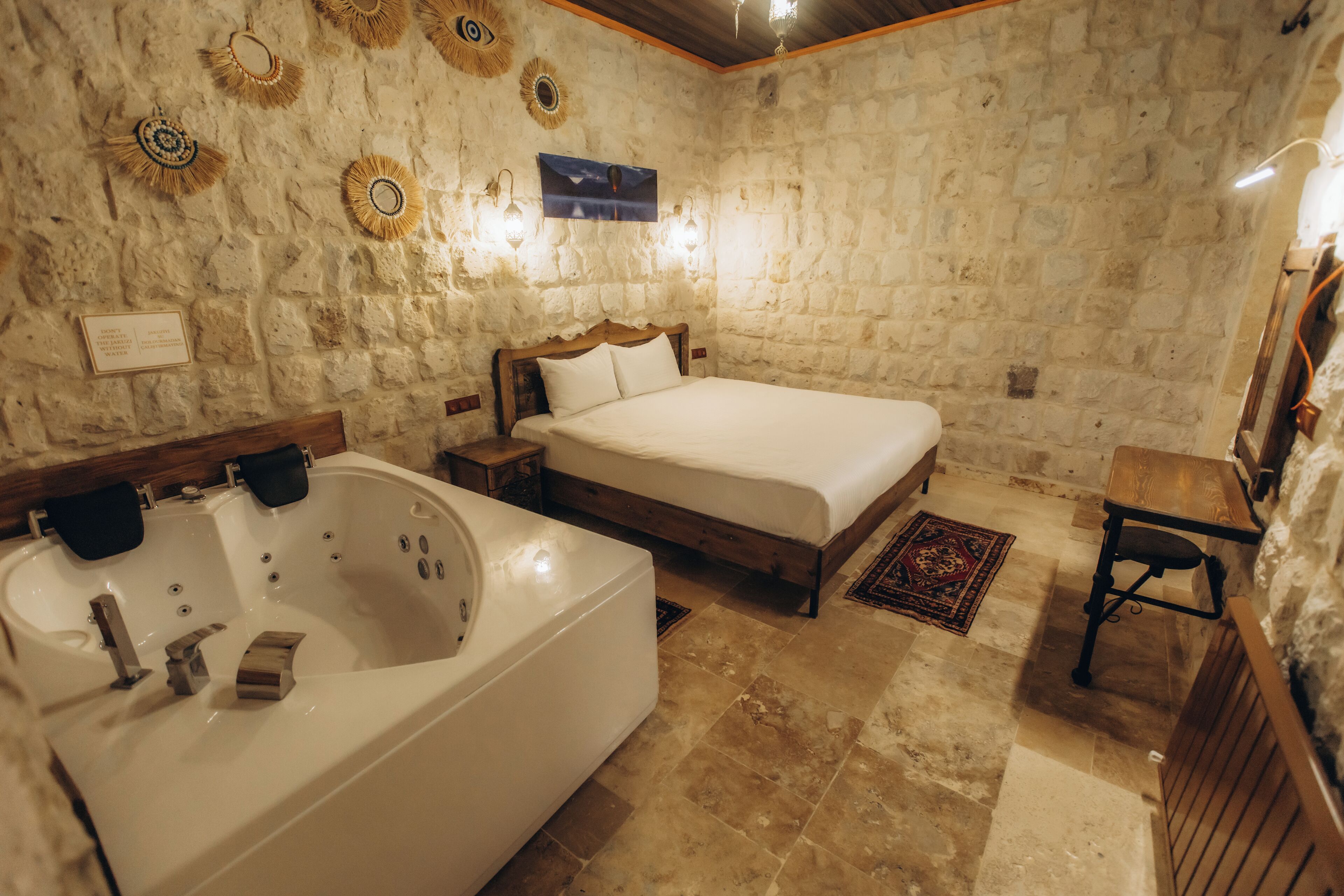 A stone-walled bedroom with a large bathtub, a wooden bed, and a small table.