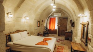 Un dormitorio con una cama grande, un banco de madera, un espejo y un tapete rojo estampado.