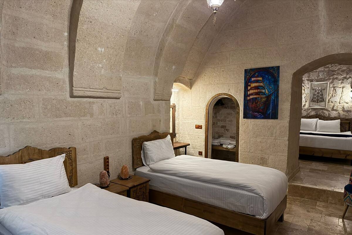 Une chambre avec deux lits, un mur en pierre, une tête de lit en bois, une petite table avec une lampe et un tableau accroché au mur.