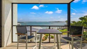 Un balcone con tavolo e due sedie, vista su un corso d'acqua e un ponte in lontananza.