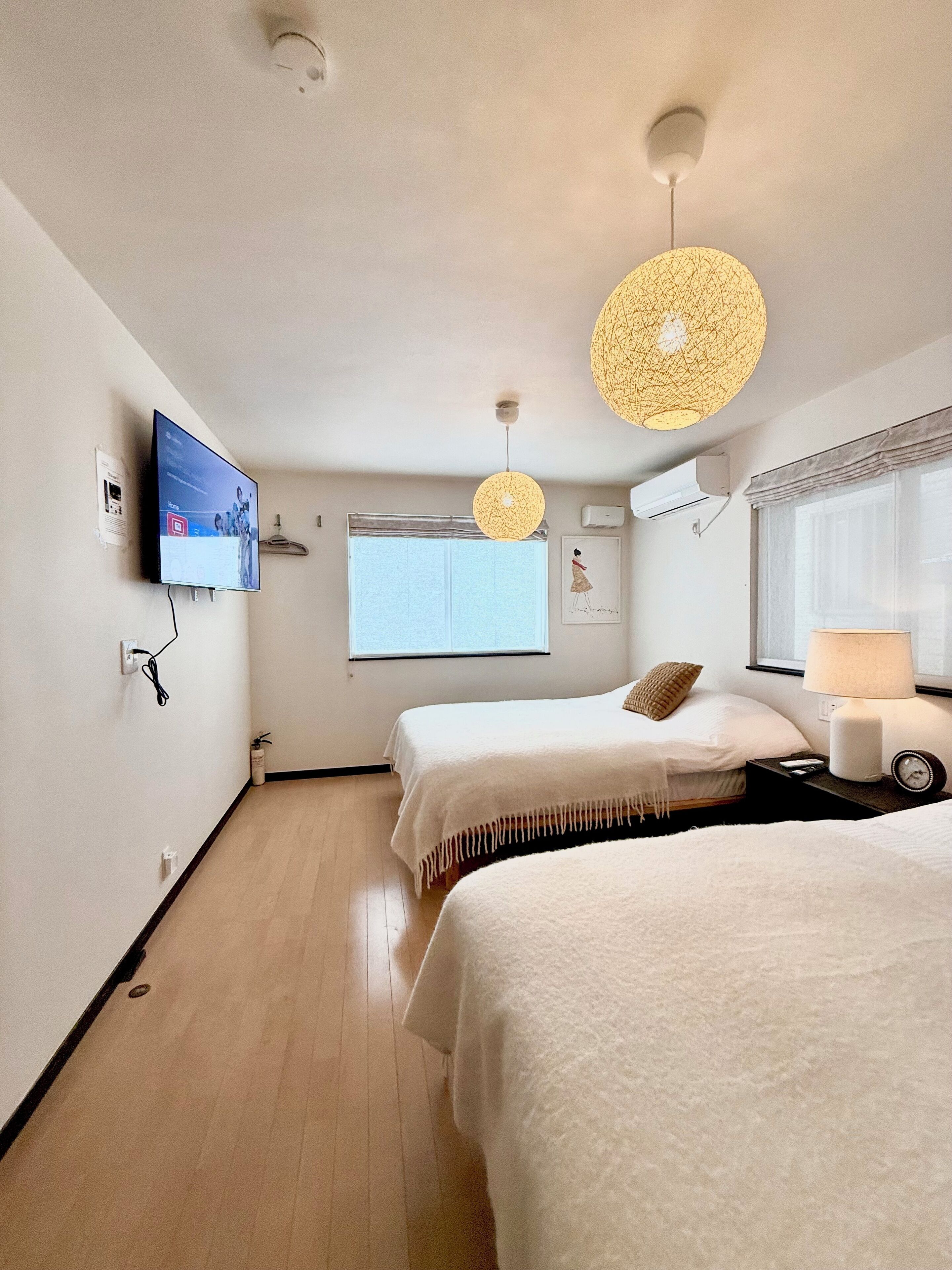 A hotel room with two beds, a TV mounted on the wall, a window with a view, and a ceiling light fixture.