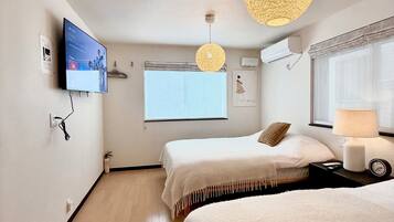 A hotel room with two beds, a TV mounted on the wall, a window with a view, and a ceiling light fixture.