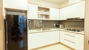 A modern kitchen with white cabinets, a black refrigerator, a microwave, and a gas stove. - Urban Oasis Apartment - Ha Do Centrosa (Ho Chi Minh City)