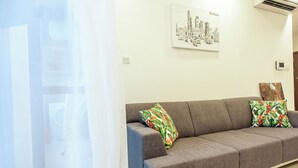 A modern living room with a grey sofa, tropical patterned pillows, and a cityscape artwork on the wall. - Urban Oasis Apartment - Ha Do Centrosa (Ho Chi Minh City)
