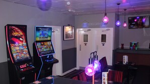Un espace bar équipé de machines à sous, d’un écran de télévision et de luminaires suspendus.